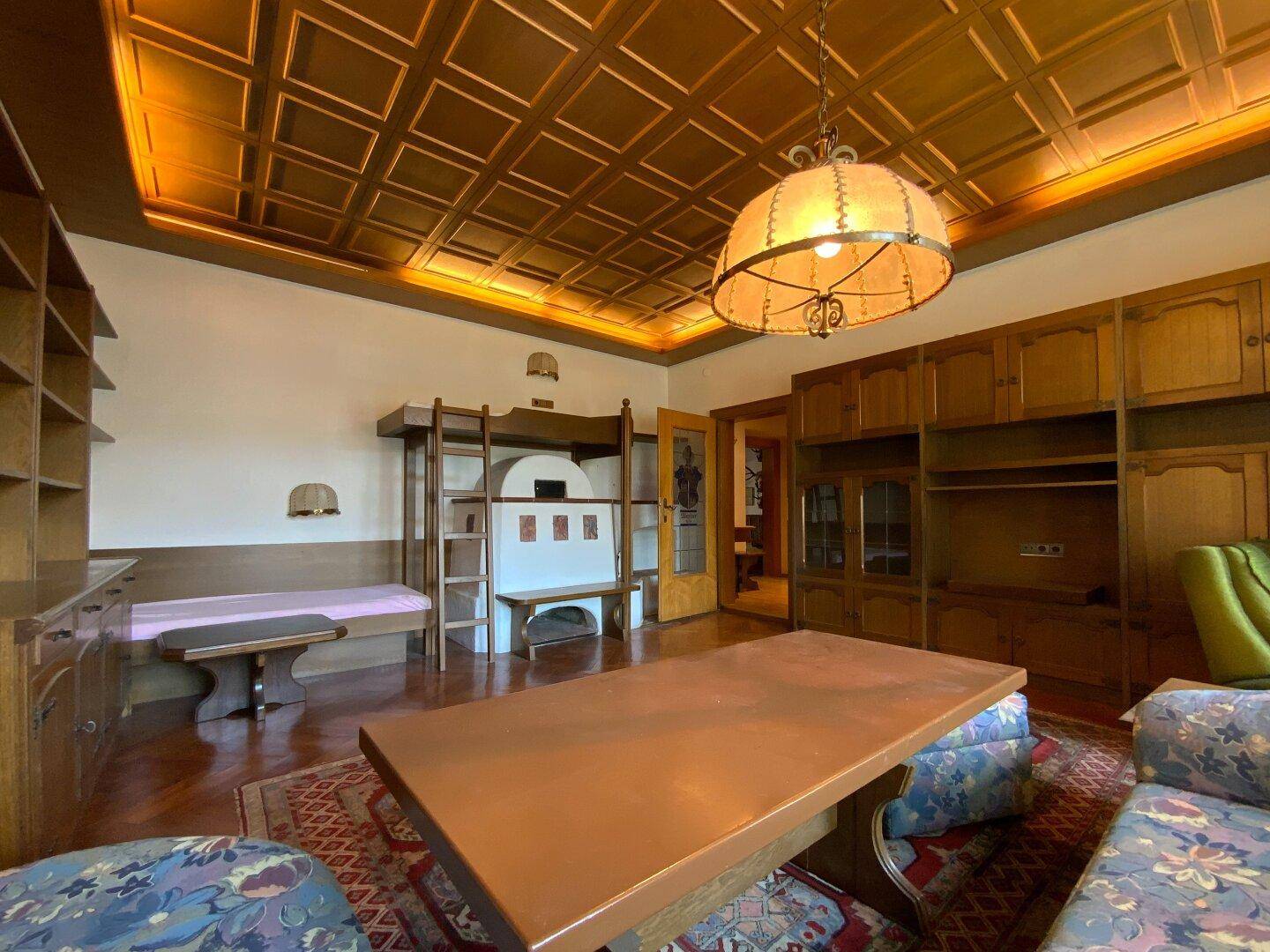 Gemütlicher Wohnbereich mit traditionellem Kachelofen, Holzmöbeln und dekorativer Decke.