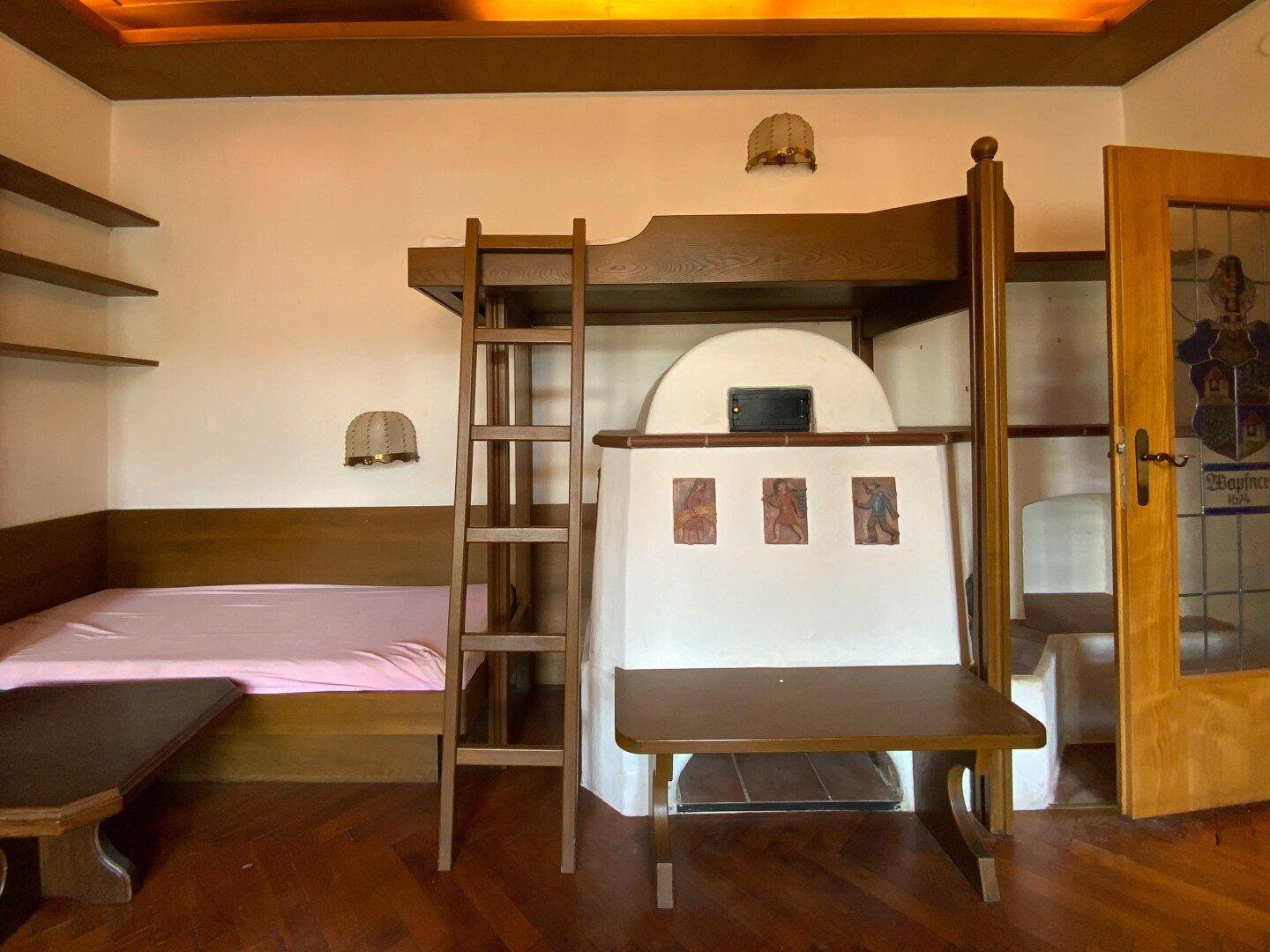 Schlafzimmer mit Kachelofen, Hochbett und Holzboden in traditionellem Stil.