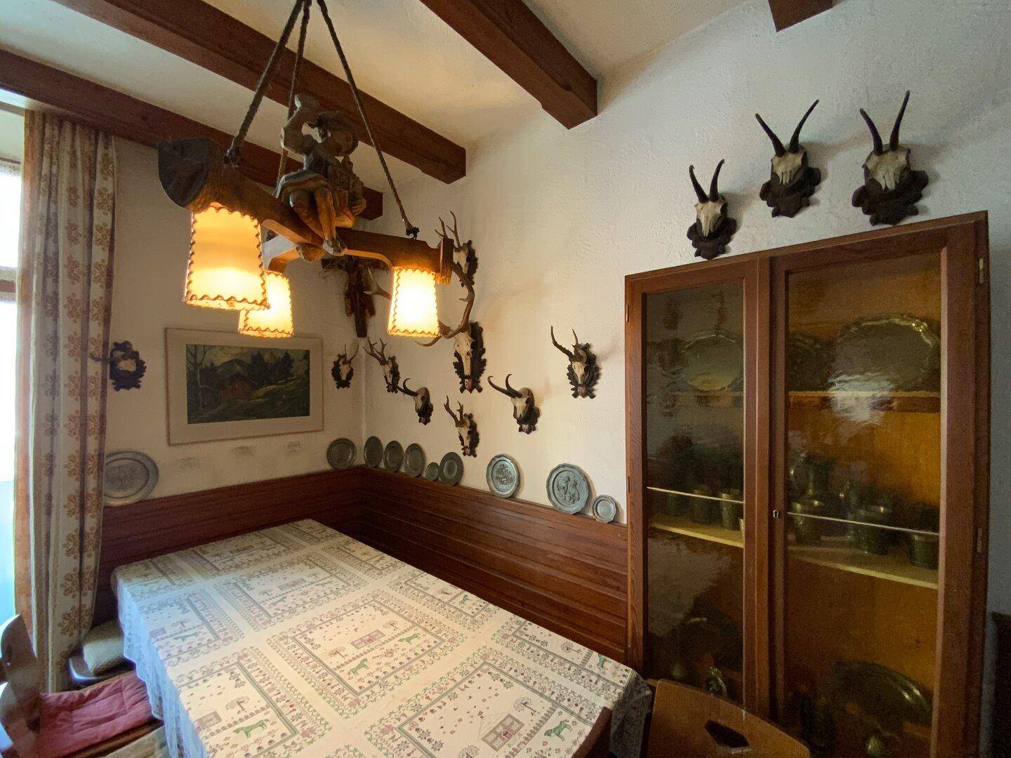 Esszimmer mit rustikalem Holzleuchter, Hirschgeweihen und einem Vitrinenschrank, traditionell eingerichtet.