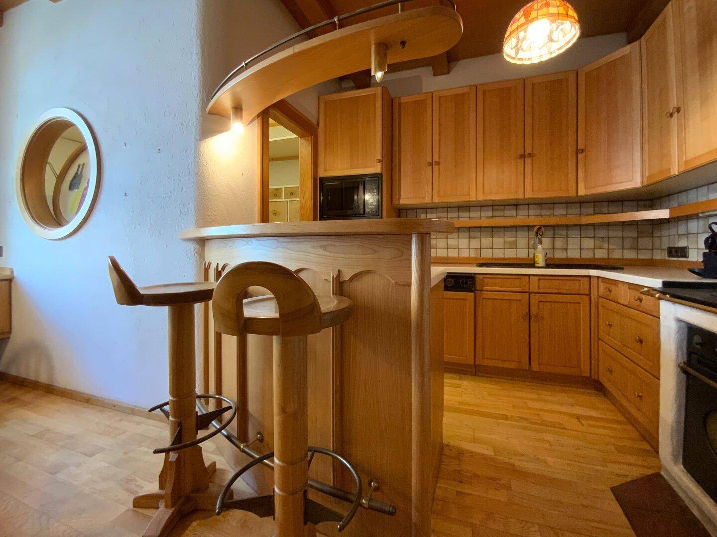 Gemütliche Holzküche mit Bartheke, Einbauschränken und traditionellem Ofen im Hintergrund, funktional und stilvoll.