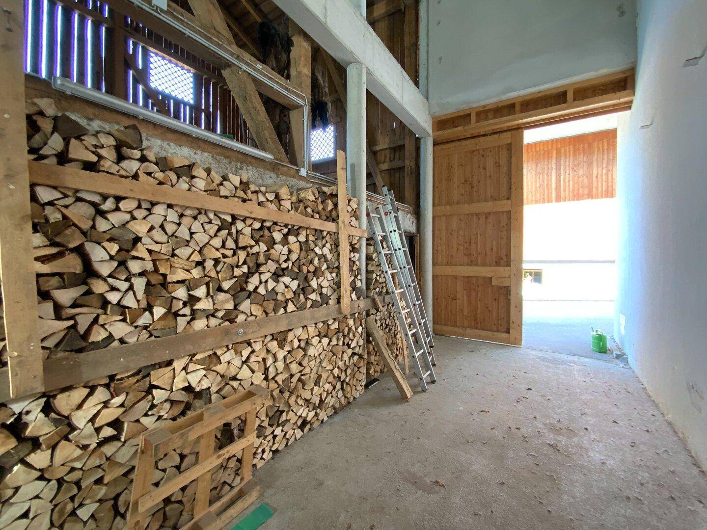Geräumiger Lagerbereich mit großen Mengen Brennholz und einem breiten Holztor.