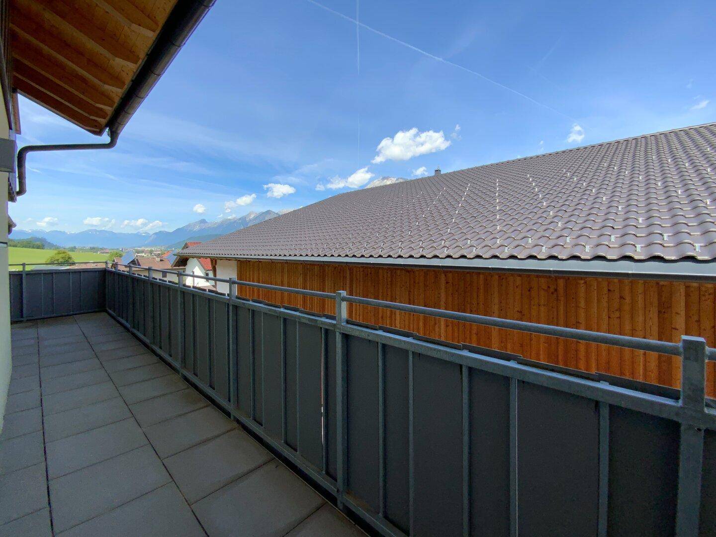 Langer Balkon mit Fliesenboden und Metallgeländer, bietet einen weiten Blick auf die Berge.