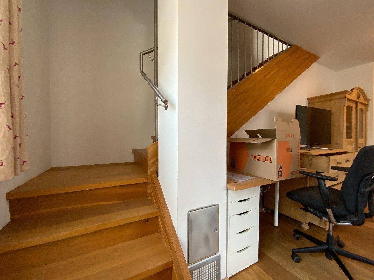 Holztreppe führt in die obere Etage, mit einem kleinen Arbeitsbereich darunter.