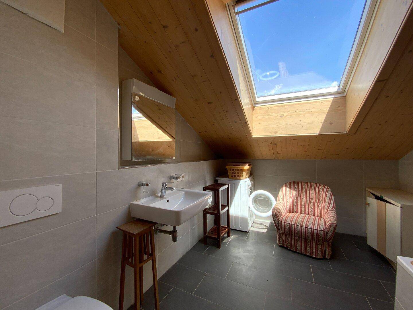 Modernes Badezimmer im Dachgeschoss mit Dachfenster, Waschbecken und Waschmaschine.