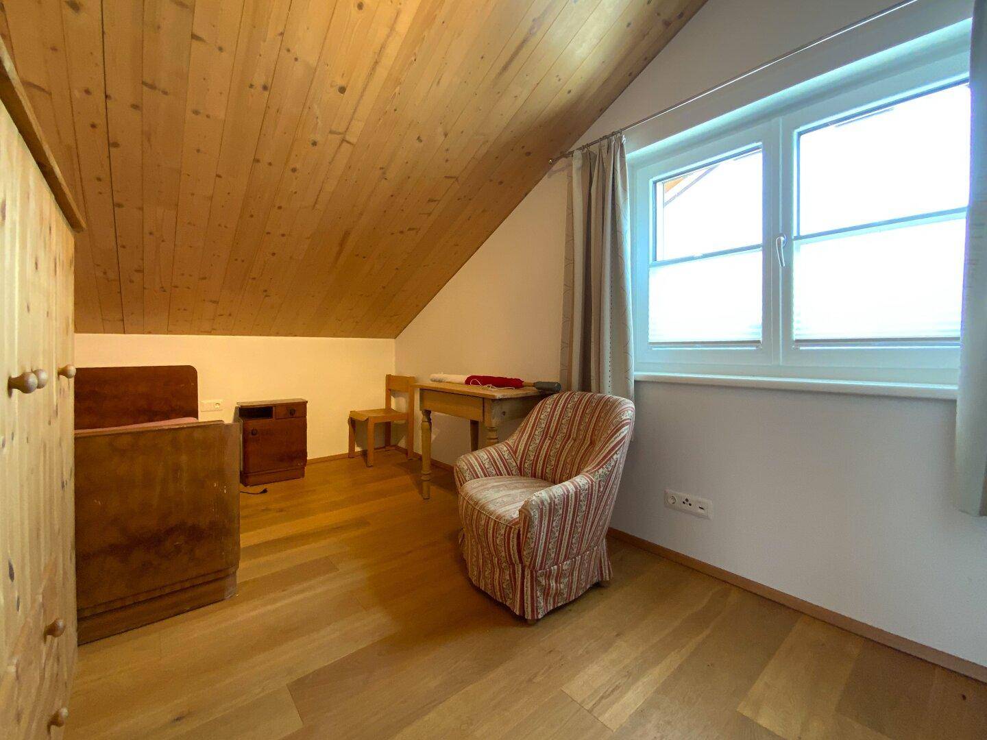 Gemütliches Schlafzimmer im Dachgeschoss mit Holzboden, Dachschräge und Fenster.