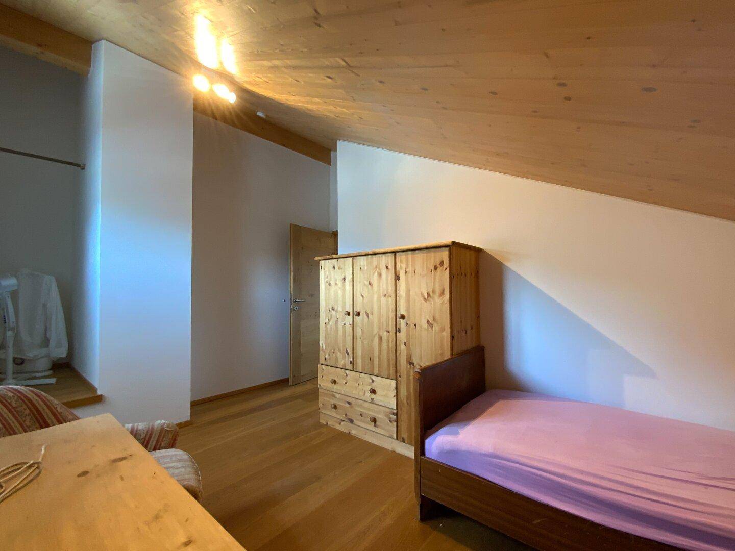 Helles Schlafzimmer mit Holzboden, Dachschräge und rustikalem Holzschrank.