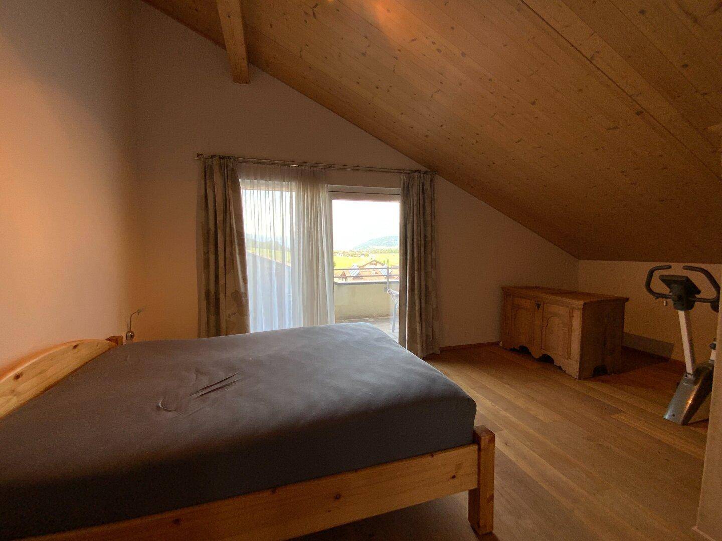 Geräumiges Schlafzimmer mit Holzboden, Zugang zum Balkon und Blick ins Grüne.