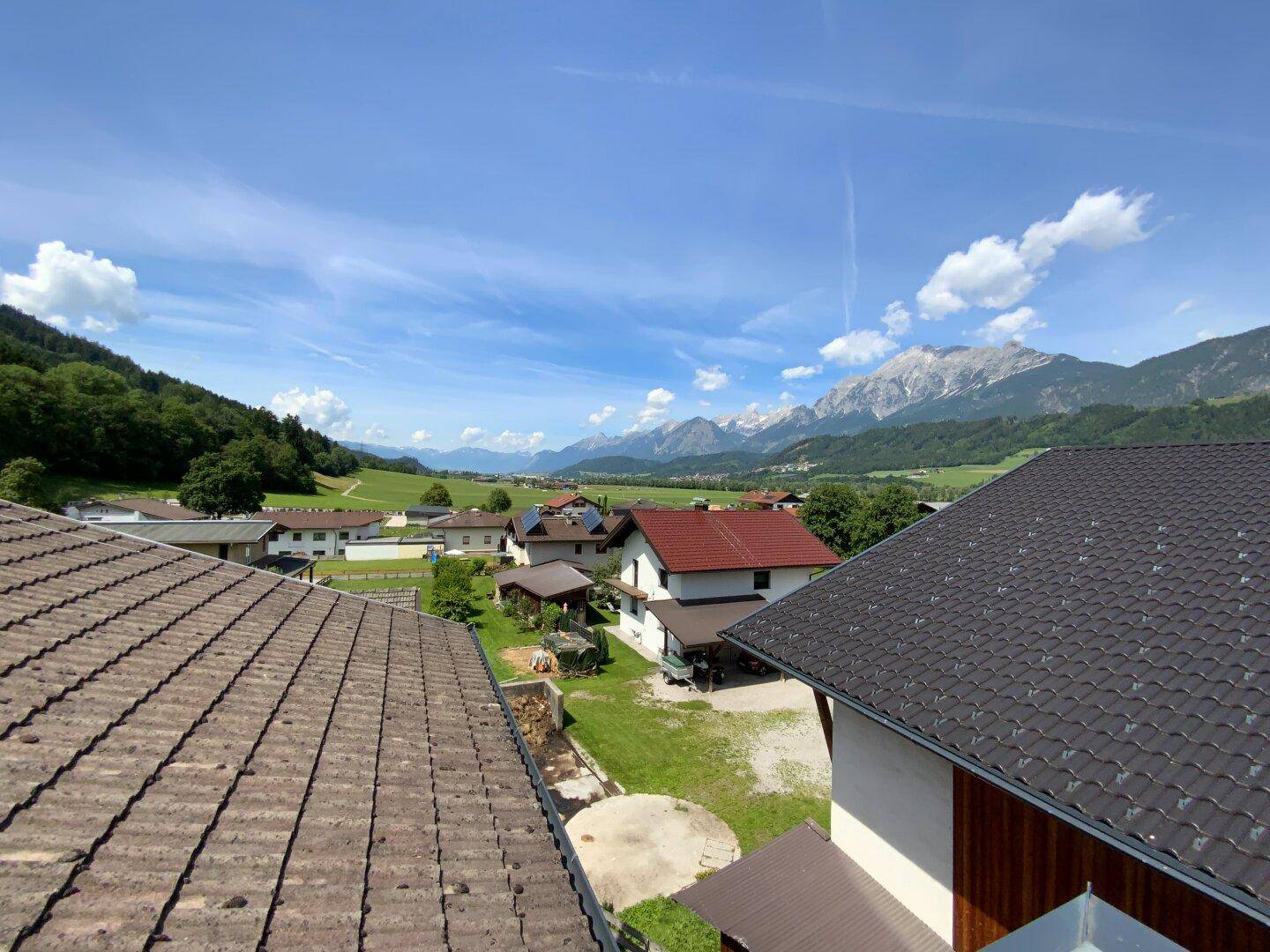 Panoramablick über die Dächer der Häuser auf eine grüne Landschaft und majestätische Berge.