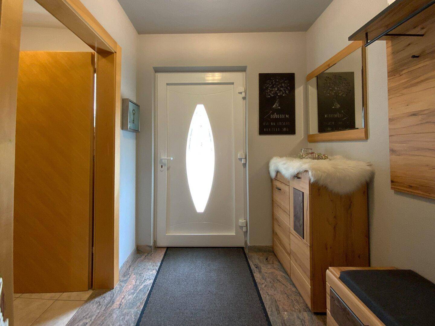 Heller Eingangsbereich mit Holzmöbeln, Spiegel und Garderobe, einladend und funktional gestaltet.