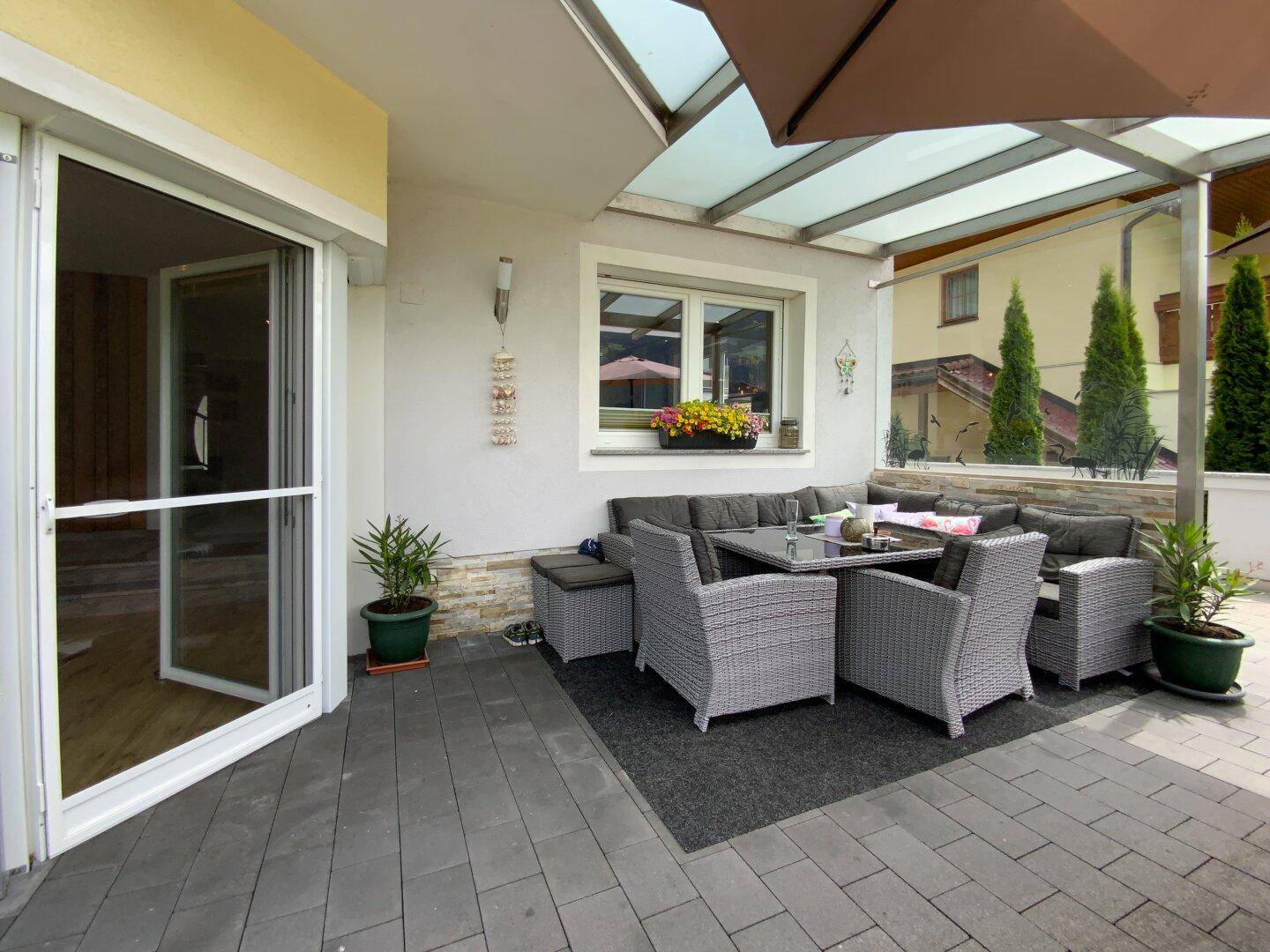 Überdachte Terrasse mit bequemen Gartenmöbeln und Glasdach, ideal für entspannte Stunden im Freien.
