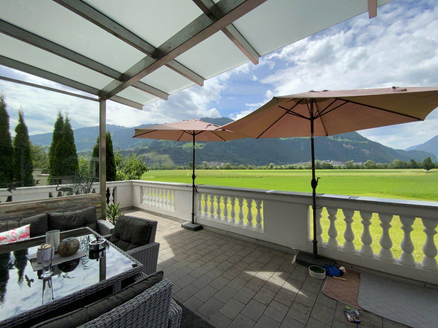 Gemütliche überdachte Terrasse mit Loungemöbeln und weitem Blick über grüne Felder und Berge.