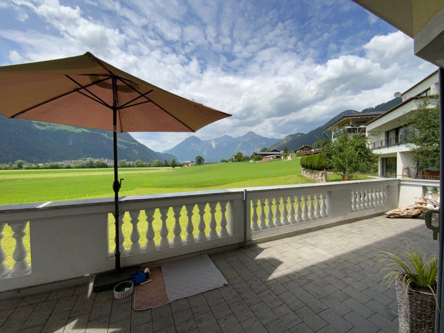 Offene Terrasse mit Sonnenschirm und weitem Blick auf die umliegende Natur und Berglandschaft.