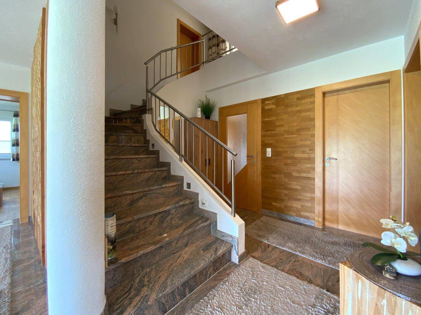 Geschwungene Treppe mit Holzvertäfelung und Natursteinboden, die den oberen Bereich erschließt.
