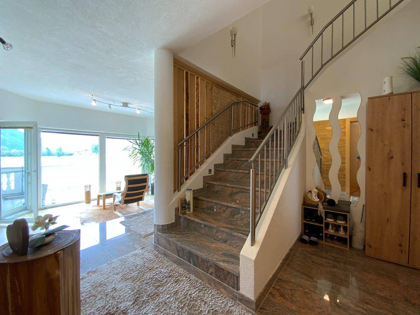 Elegante Treppe mit Edelstahlgeländer und Natursteinfliesen, die die verschiedenen Ebenen verbindet.
