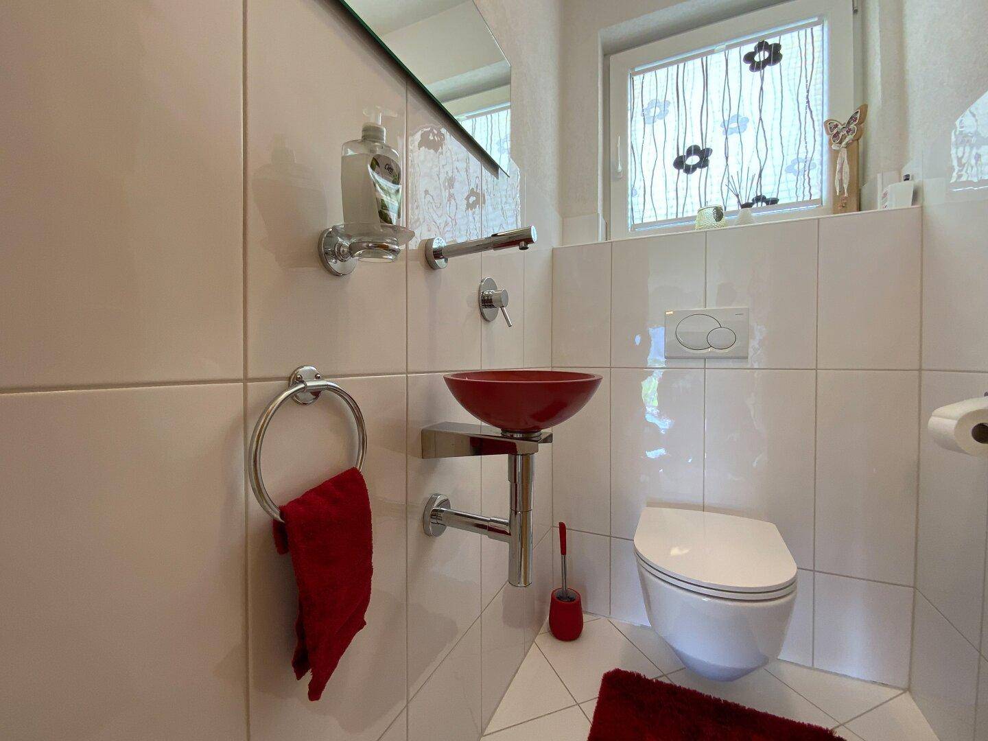 Modernes Gäste-WC mit weißen Fliesen, rotem Waschbecken und wandhängender Toilette.