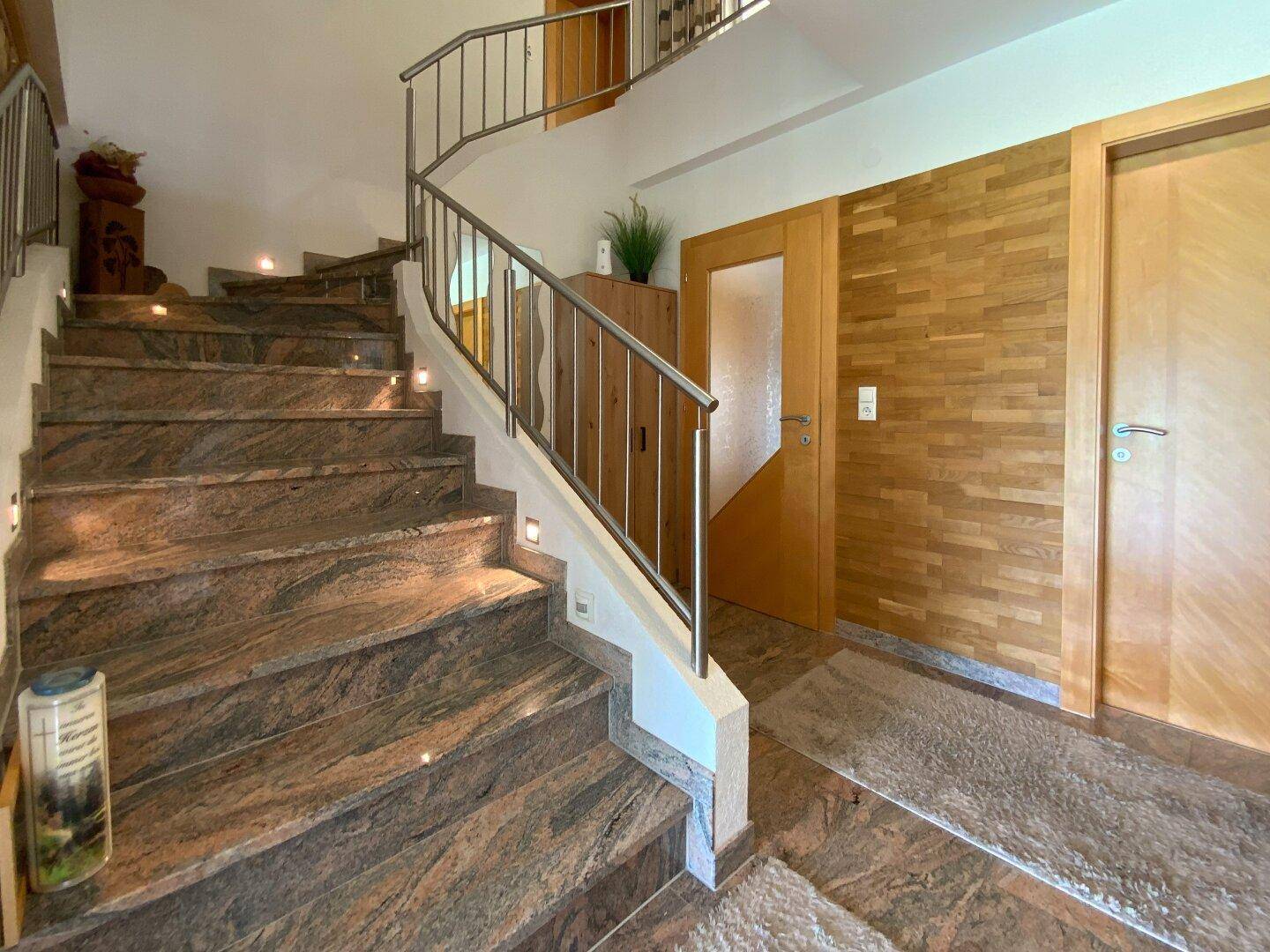 Elegante Treppe mit Natursteinbelag und modernem Metallgeländer in einem hellen Eingangsbereich.