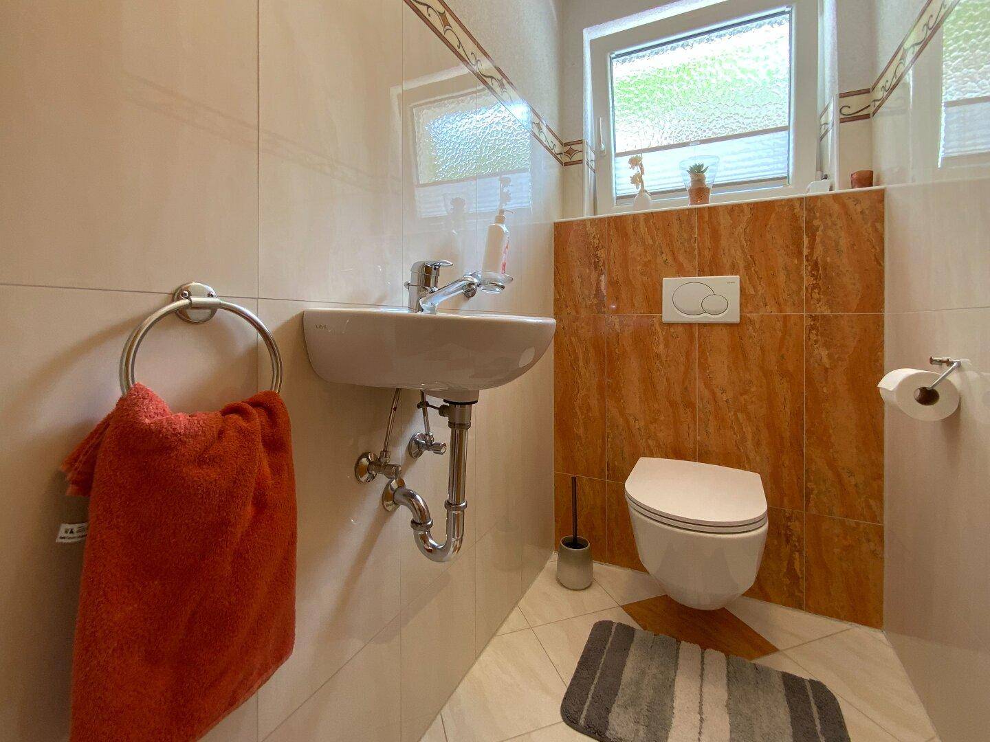 Helles Gäste-WC mit beigen Fliesen, weißem Waschbecken und Fenster für Tageslicht.