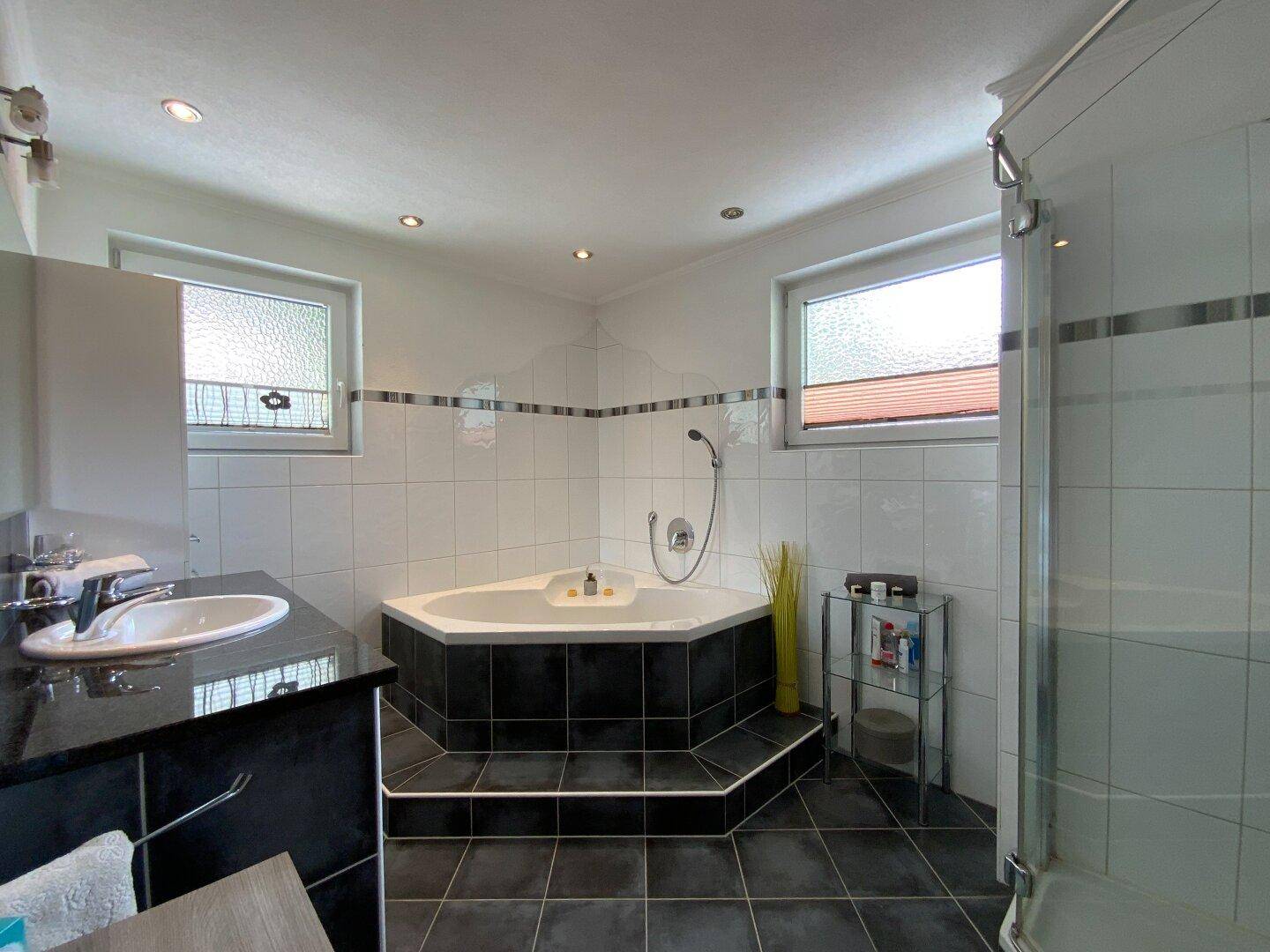 Modernes Badezimmer mit Eckbadewanne, separater Dusche und dunklen Fliesen, gut beleuchtet.