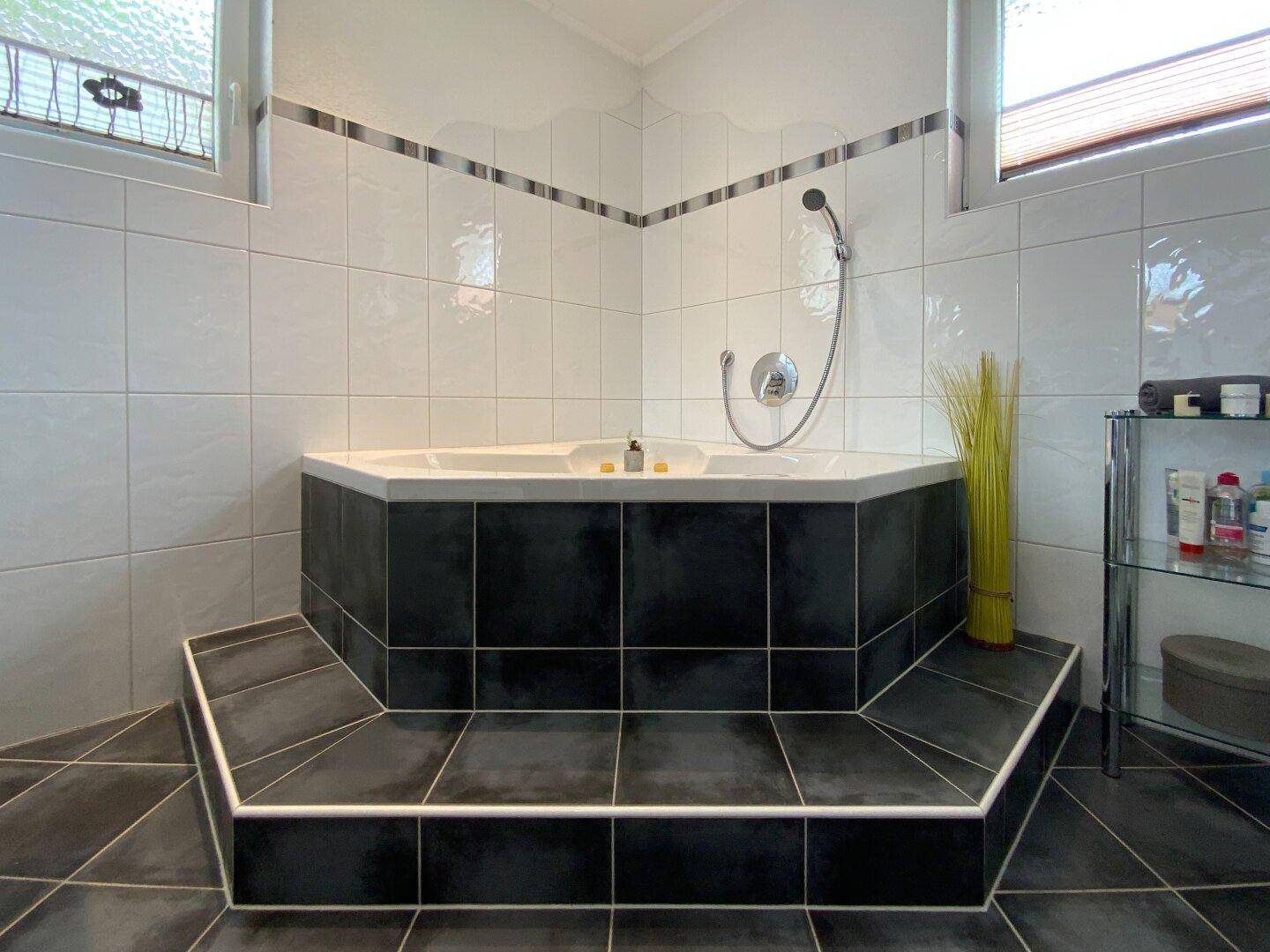 Elegante Eckbadewanne mit dunklen Fliesen und weißer Umrandung, ideal für entspannende Bäder.