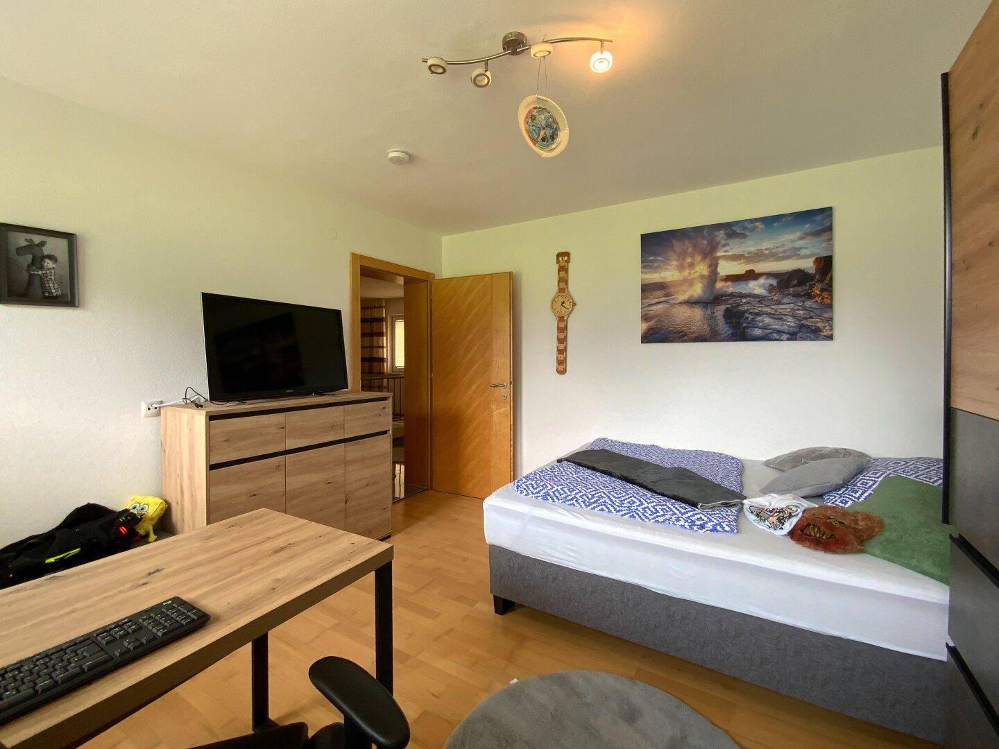 Komfortables Schlafzimmer mit Holzboden, Schreibtisch und dekorativen Elementen für eine angenehme Atmosphäre.
