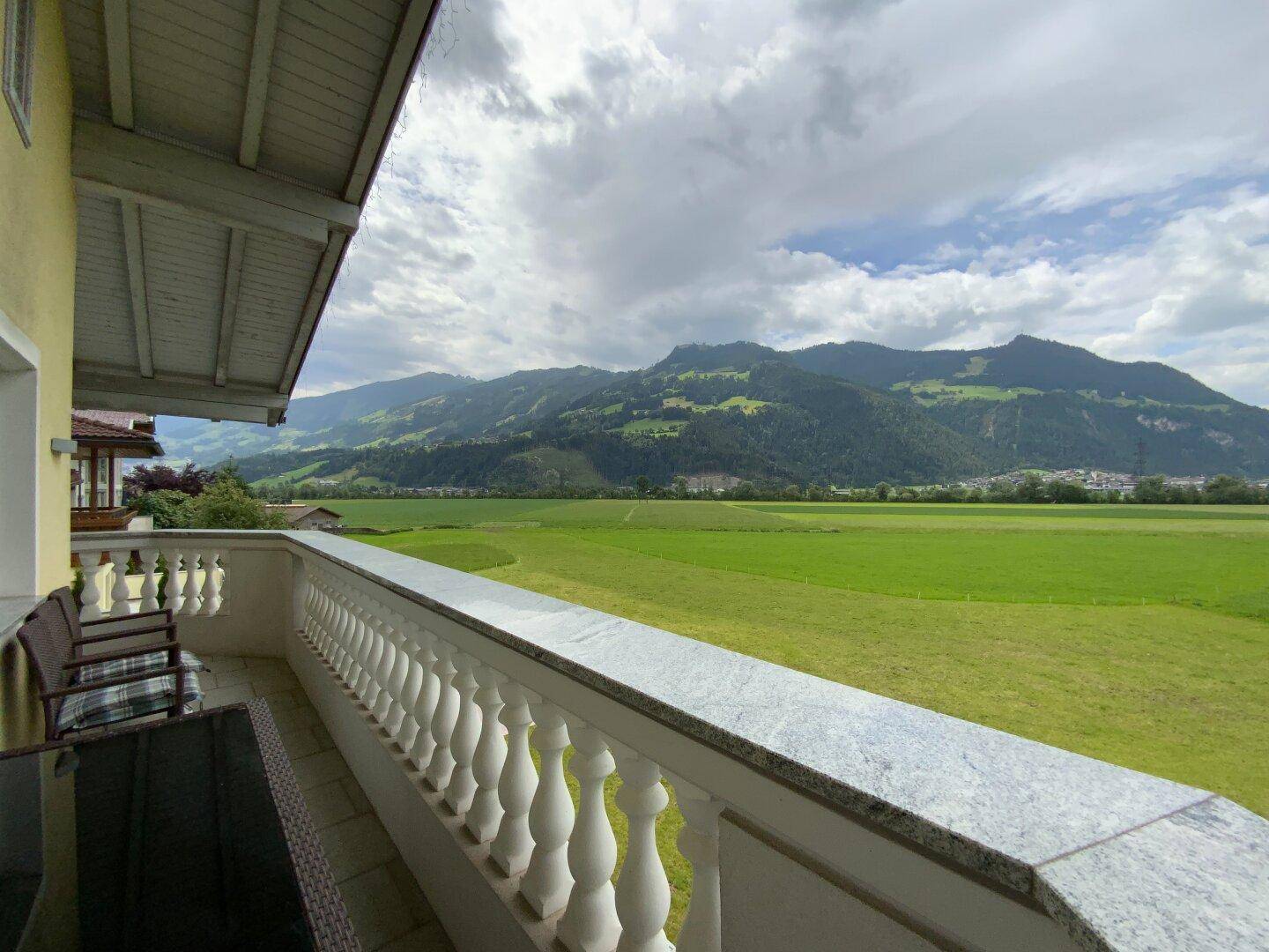 Großer Balkon mit Sitzgelegenheiten und atemberaubendem Blick auf grüne Felder und die umliegenden Berge.