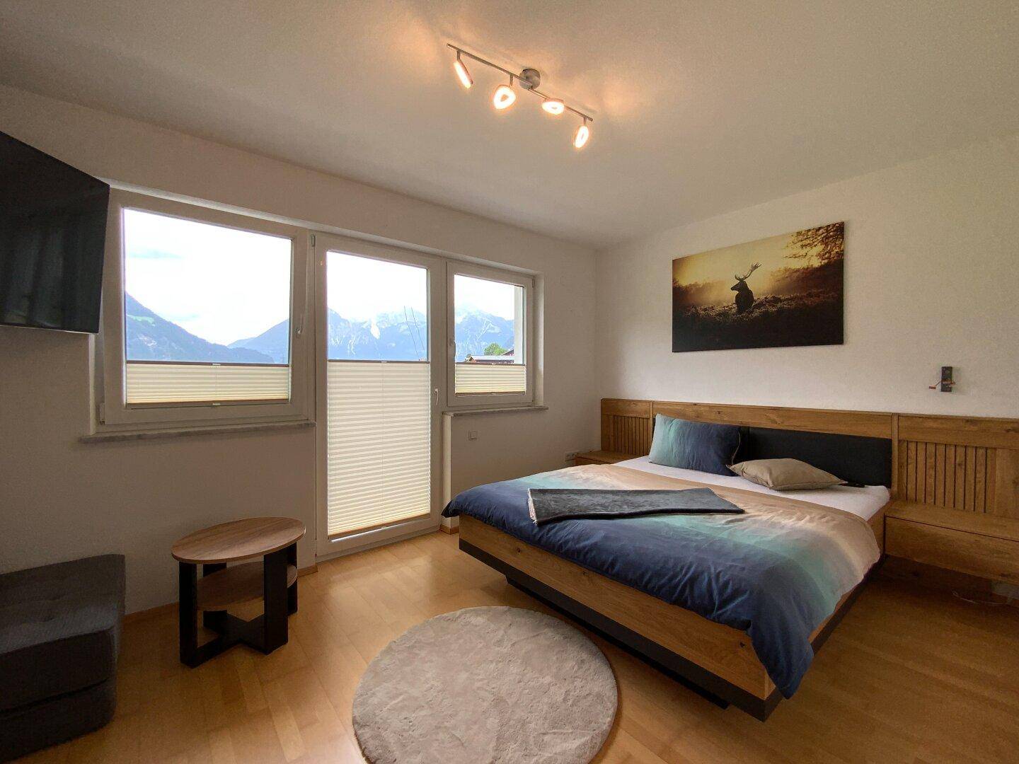 Helles Schlafzimmer mit Holzboden, modernem Bett und beeindruckendem Bergblick durch die Fenster.