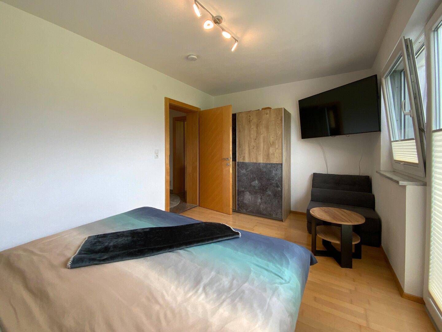 Funktionales Schlafzimmer mit Holzboden, geräumigem Kleiderschrank und wandmontiertem Fernseher.