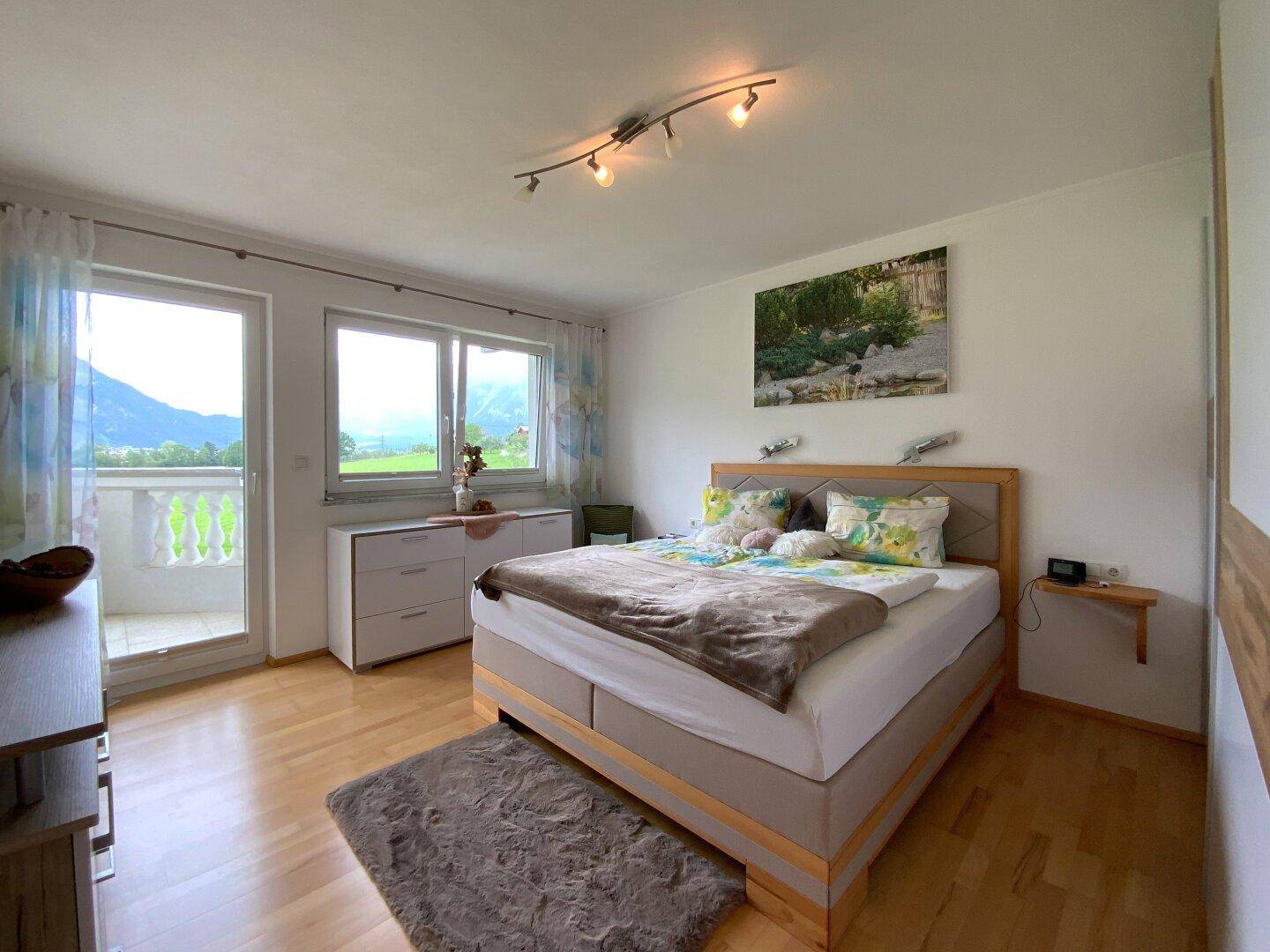 Helles Schlafzimmer mit Holzboden, Doppelbett und direktem Zugang zu einem Balkon mit Bergblick.