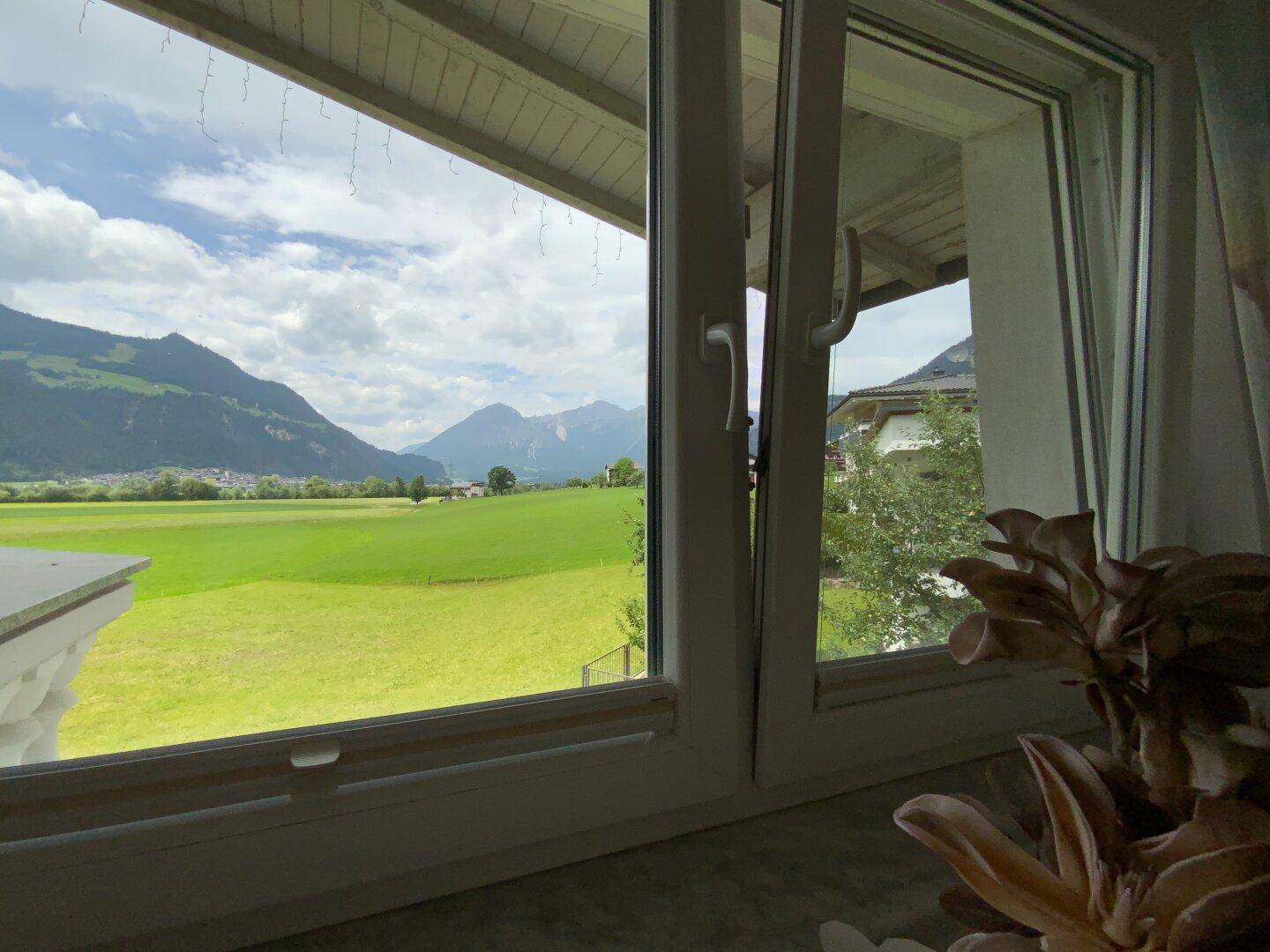 Weitläufiger Blick aus dem Fenster über grüne Wiesen und eine beeindruckende Berglandschaft.
