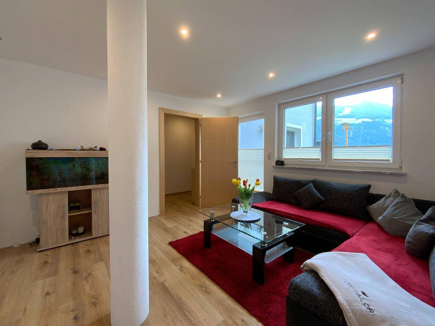 Helles Wohnzimmer mit bequemer Sitzecke, Couchtisch und Fenstern, die viel Tageslicht hereinlassen.
