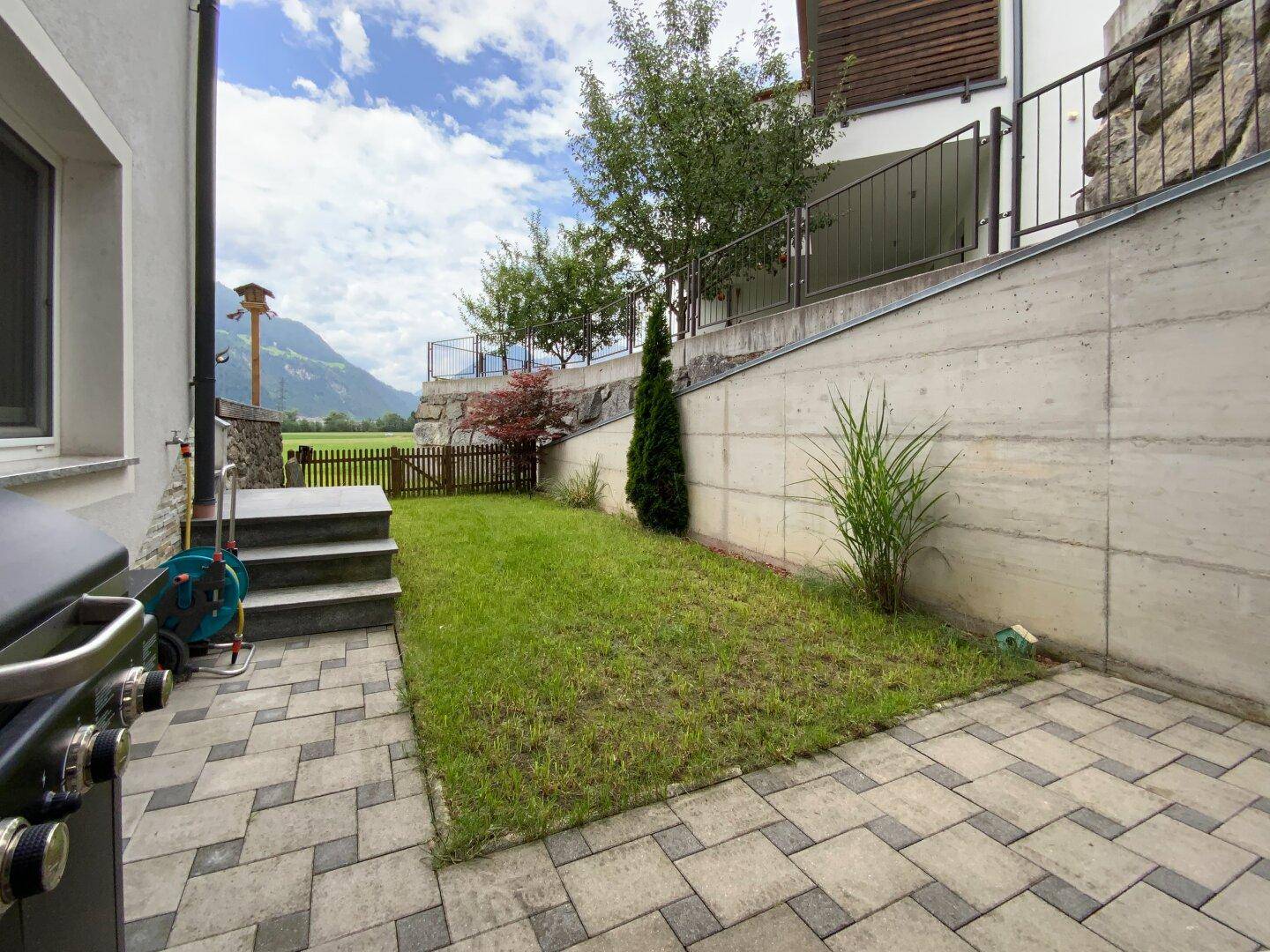 Kleiner, gepflegter Garten mit gepflasterter Terrasse, Rasenfläche und Grillbereich für gemütliche Abende.