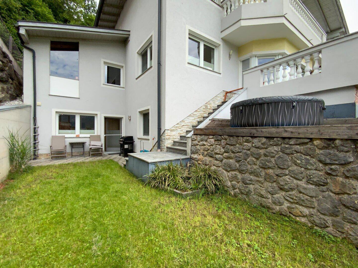 Gepflegter Gartenbereich mit Rasenfläche, gepflastertem Sitzplatz und einem aufblasbaren Whirlpool.