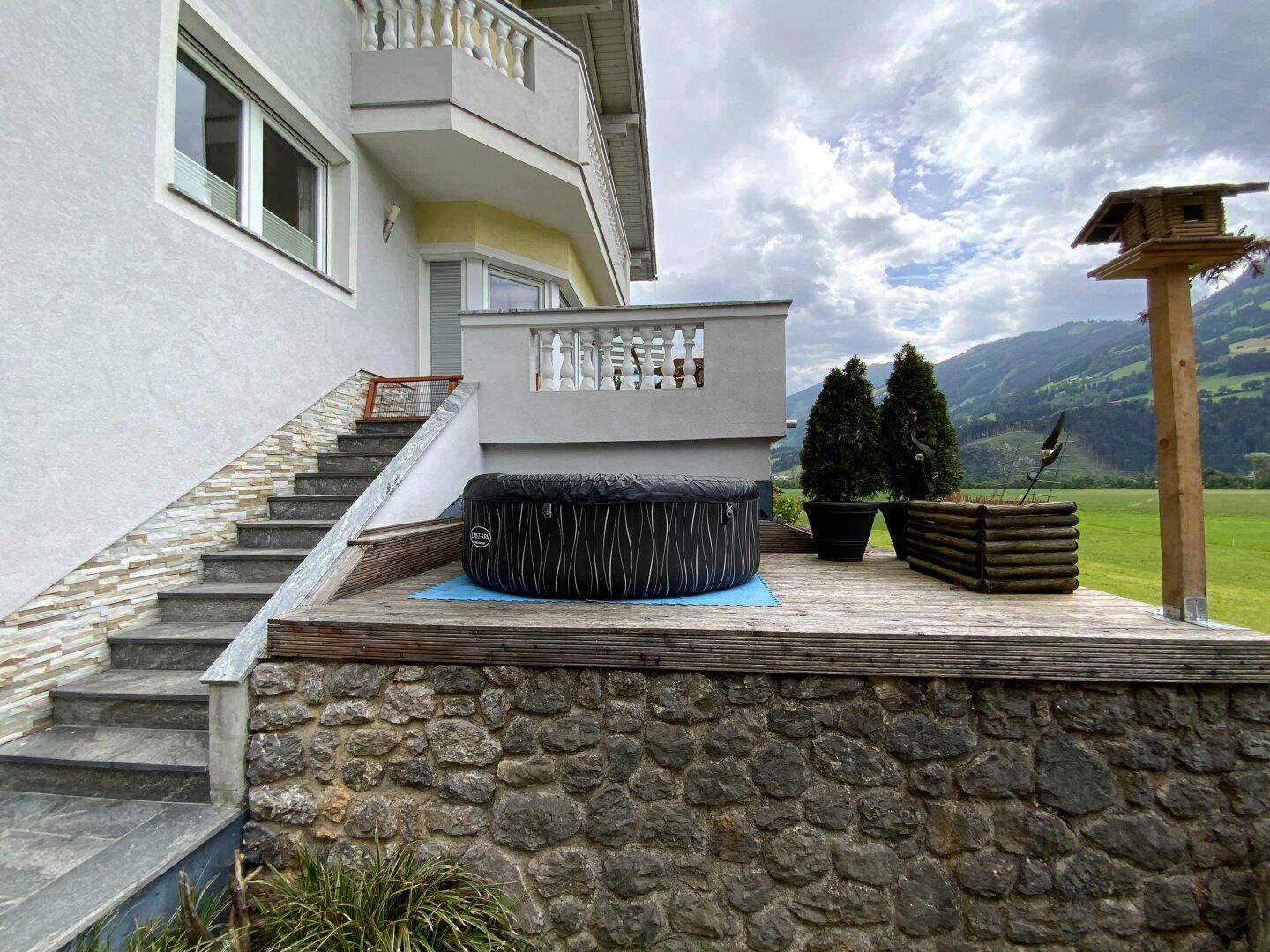 Holzterrasse mit aufblasbarem Whirlpool und Treppe, die zum oberen Balkon des Hauses führt.