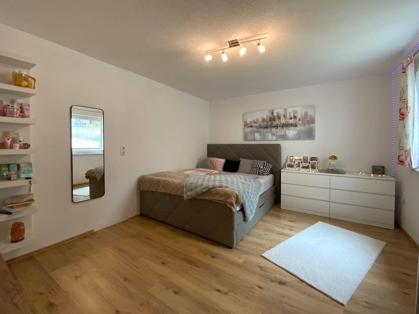 Modernes Schlafzimmer mit Doppelbett, weißer Kommode und offenen Regalen für persönlichen Stauraum.