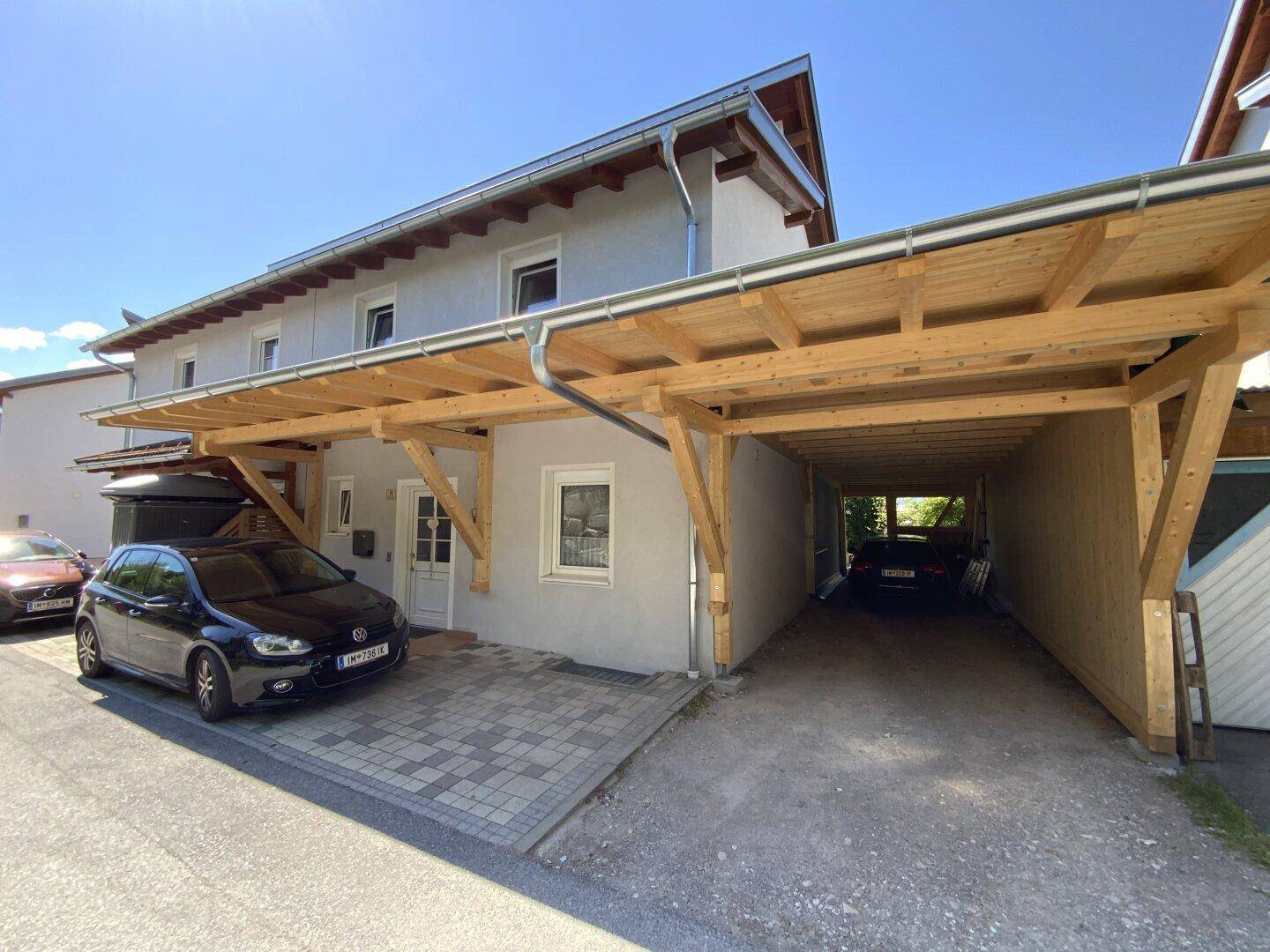 Hausfassade mit einem großen hölzernen Carport, der Parkmöglichkeiten bietet.