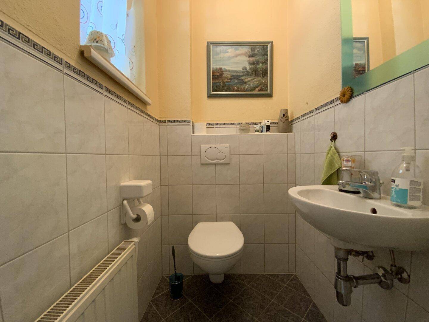 Kleines Gäste-WC mit Toilette, Waschbecken und einem Fenster für natürliche Belüftung.
