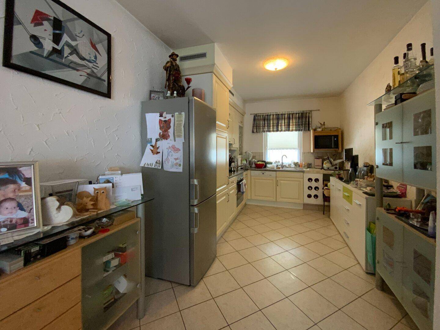 Funktionale Küche mit cremefarbenen Einbauschränken, Fliesenboden und Fenster.