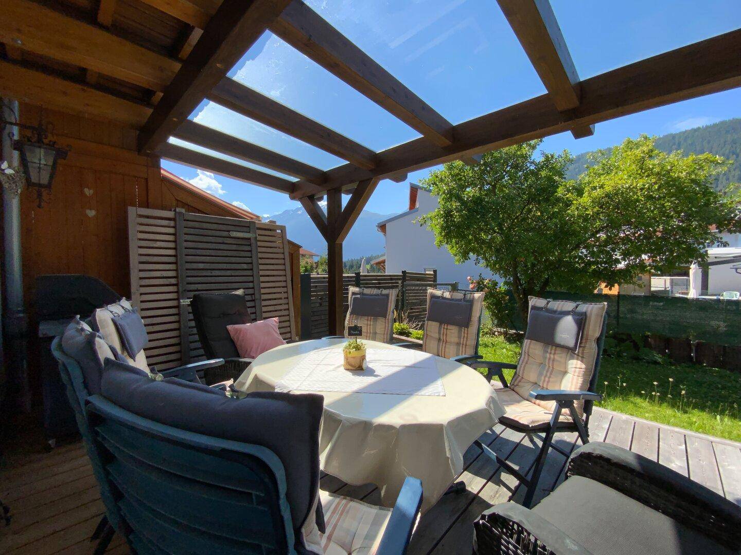 Überdachte Holzterrasse mit Esstisch und Stühlen, ideal für Mahlzeiten im Freien.