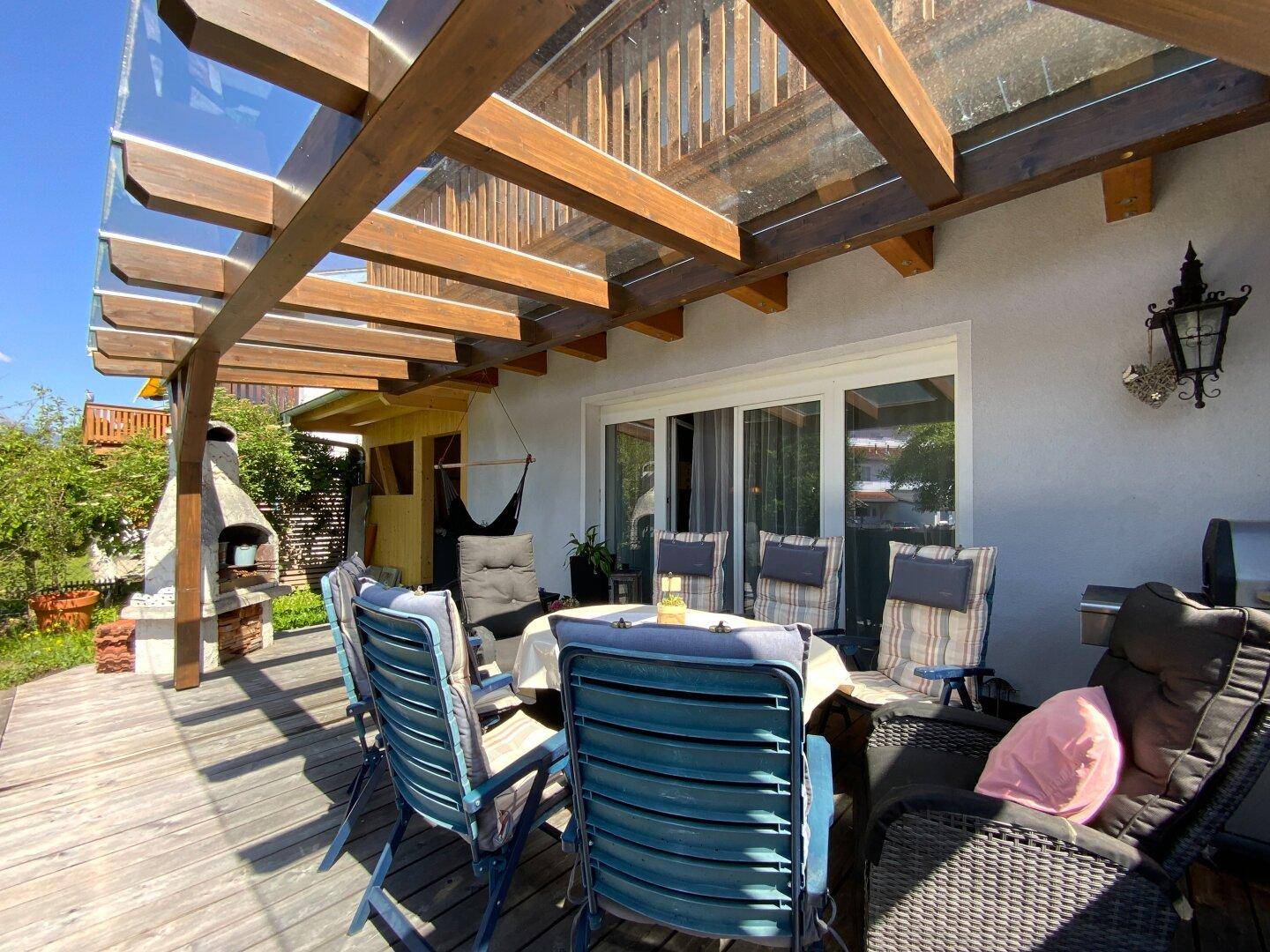 Sonnige Terrasse mit bequemen Gartenmöbeln und Blick auf den Grillbereich und das Haus.