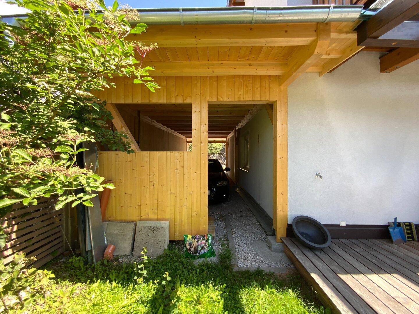 Seitenansicht des Hauses mit hölzernem Carport und einem kleinen Gartenbereich.