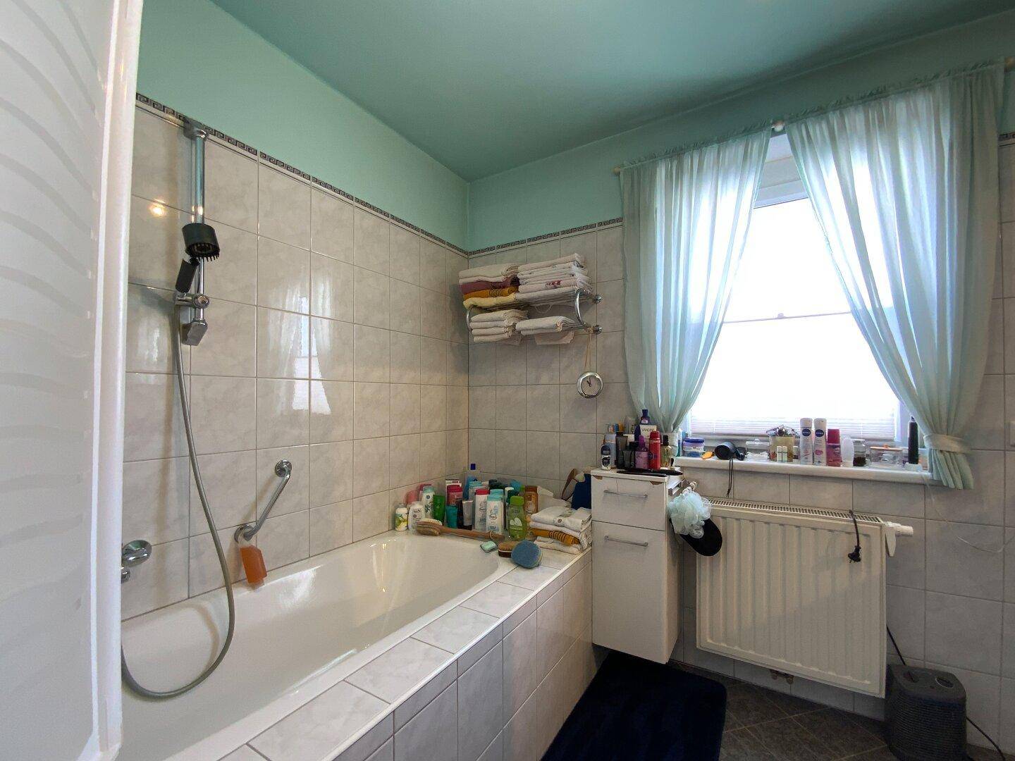 Badezimmer mit Badewanne, hellen Fliesen und einem Fenster für Tageslicht.