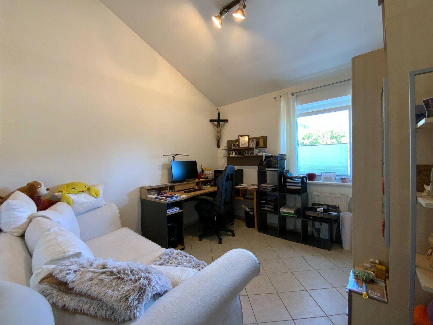 Vielseitiger Raum mit Sofa, Schreibtisch und Dachschräge, ideal als Büro oder Gästezimmer.