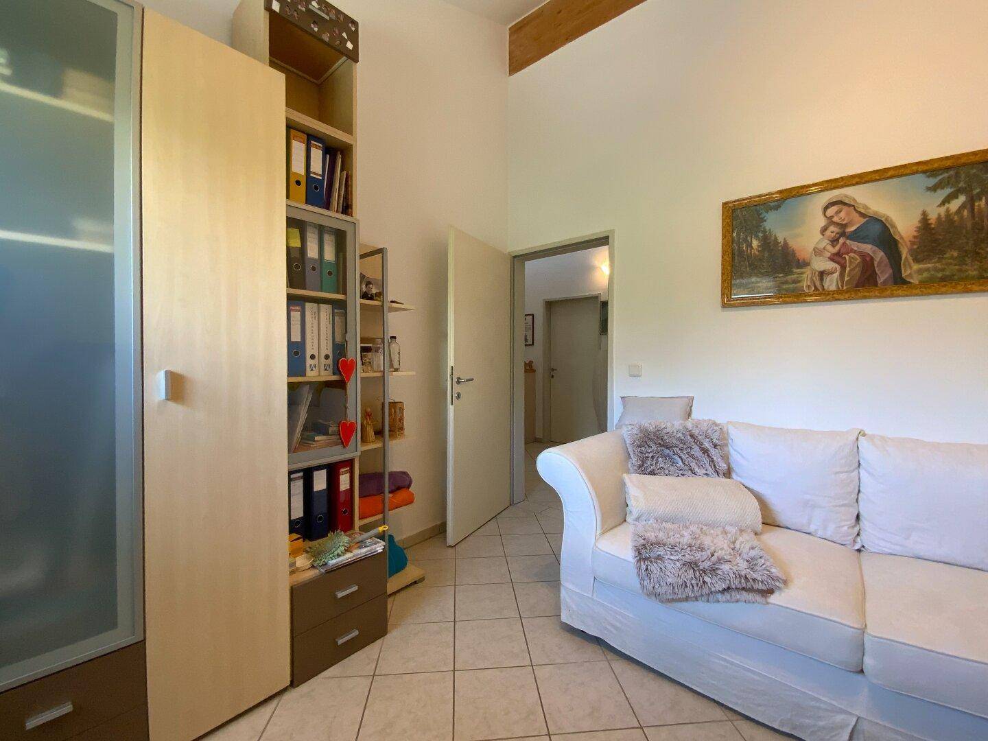 Heller Raum mit weißem Sofa, Regalsystem und sichtbaren Holzbalken an der Decke.