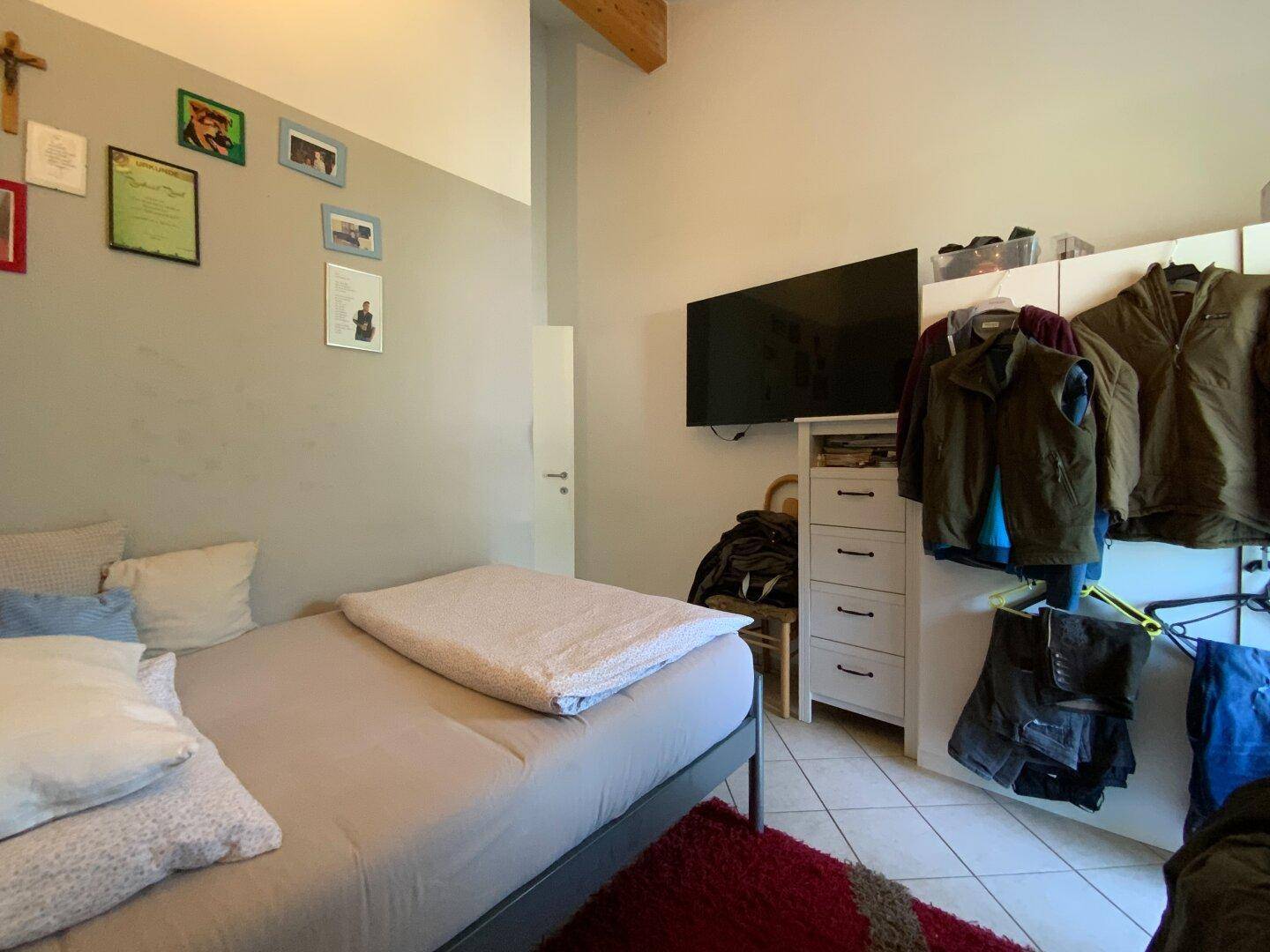 Gemütliches Schlafzimmer mit Einzelbett, Fliesenboden und einem Fernseher an der Wand.