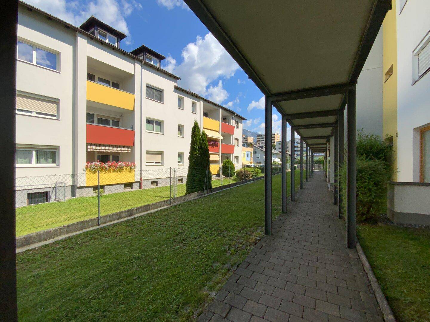 Wohngebäude mit farbenfrohen Balkonen, langem überdachtem Gang und weitläufiger Rasenfläche.