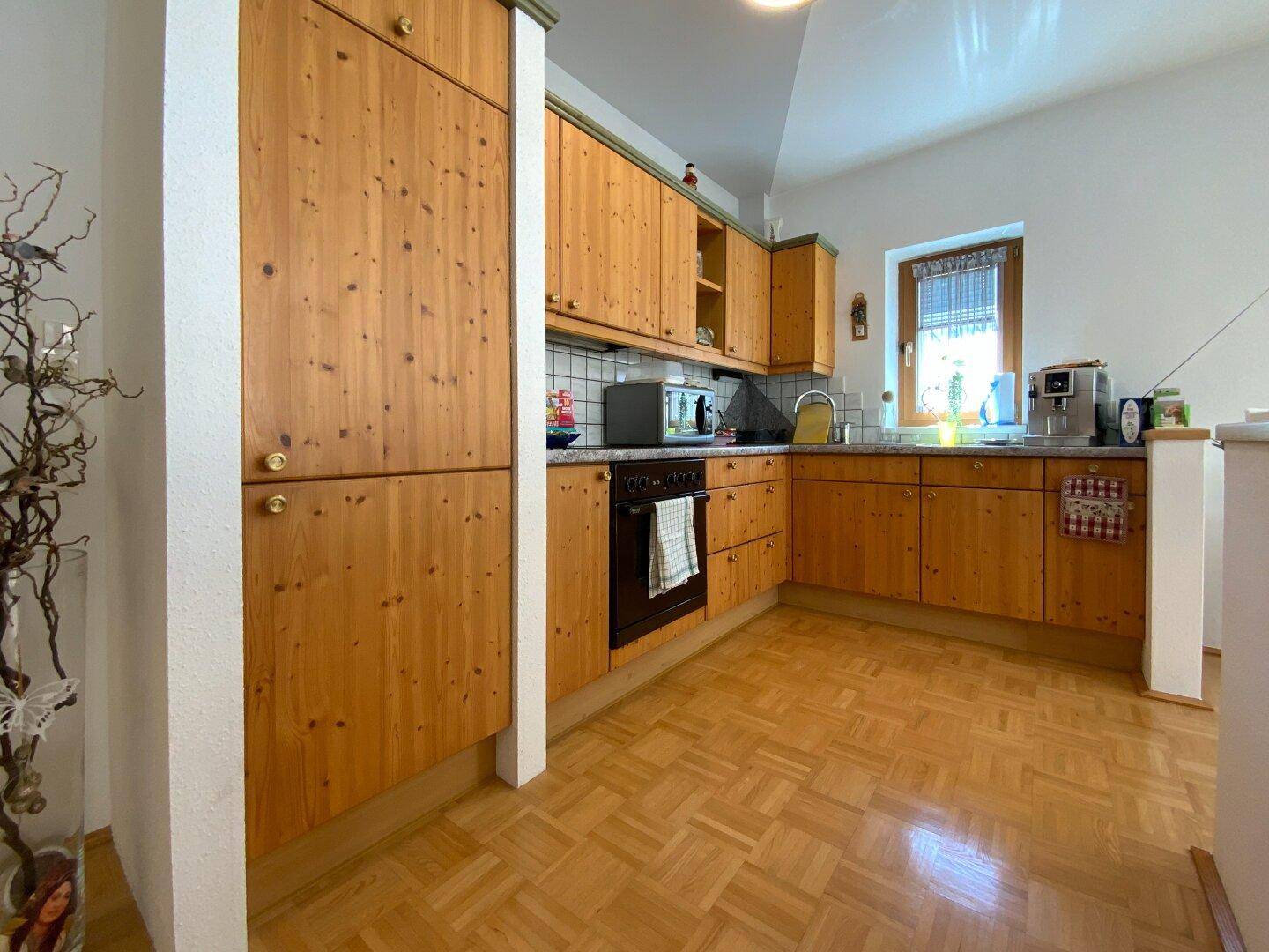 Funktionale Küche mit hellen Holzschränken, Backofen und Fenster für Tageslicht.