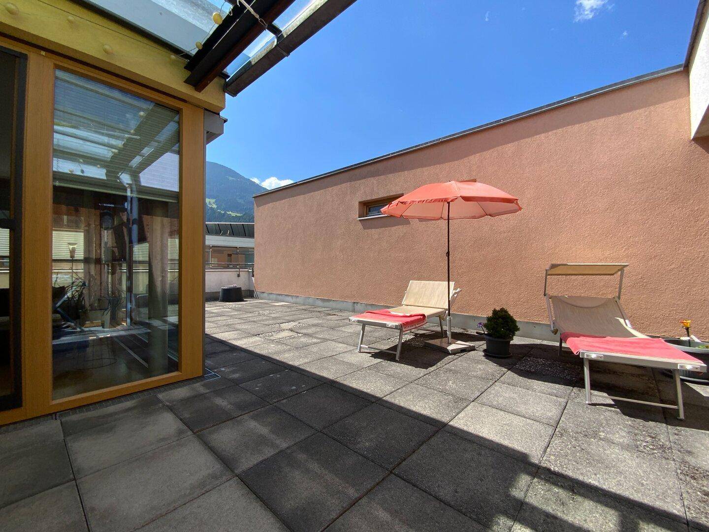 Großzügige Sonnenterrasse mit Liegestühlen und Sonnenschirm, ideal zum Entspannen.