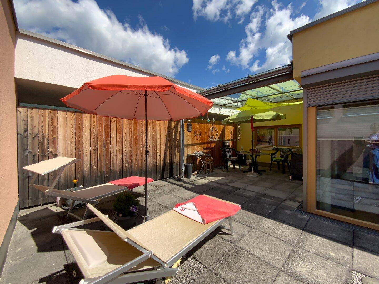 Weitläufige Terrasse mit Liegestühlen, Sonnenschirm und Blick auf einen weiteren Sitzbereich.