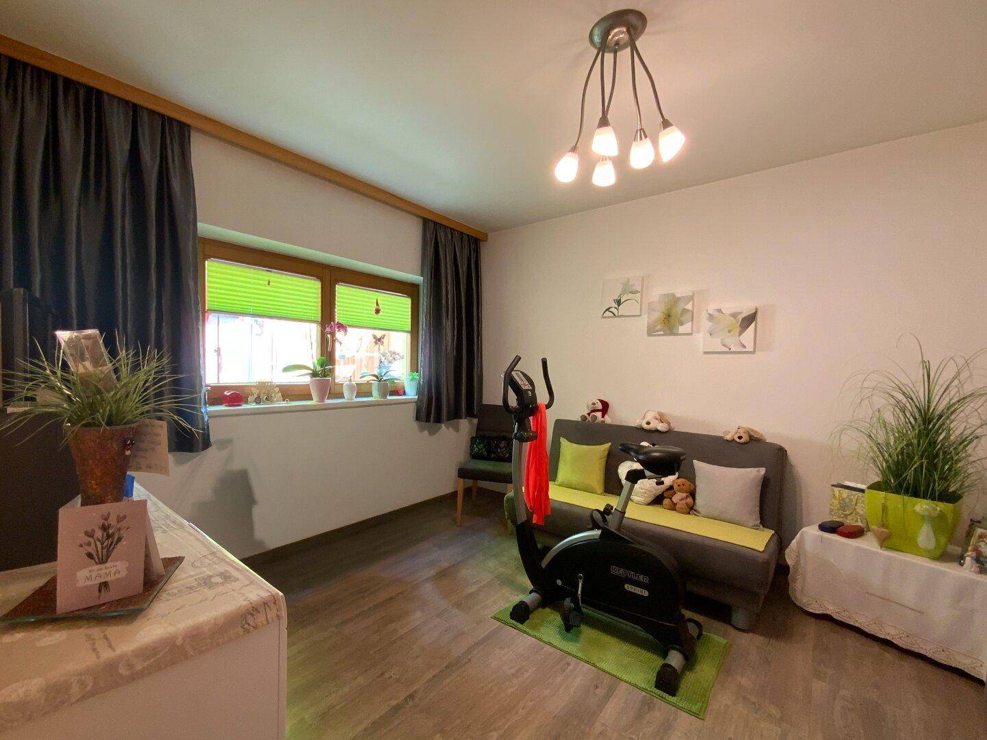 Vielseitig nutzbarer Raum mit Sofa, Trainingsgerät und Fenster mit Blick ins Grüne.