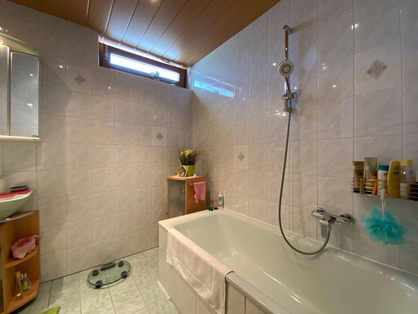 Badezimmer mit Badewanne, Waschbecken und hellen Fliesen, ausgestattet mit einem kleinen Fenster.